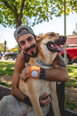 Happy, healthy and fit young latin man with tattooed upper arm and shoulder, cap and purple shirt hugging his beautiful german shepherd friend dog in an street workout park in a sunny day