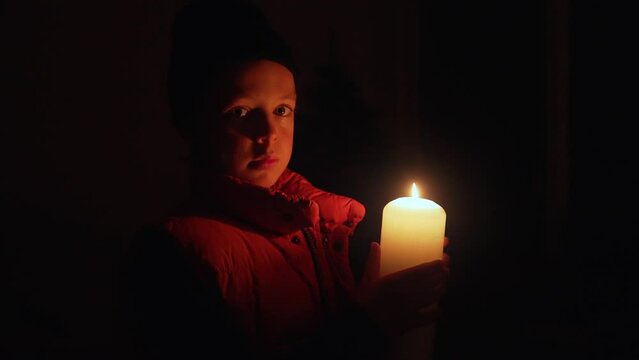 Boy at home during a blackout in Ukraine holding candle in complete darkness.