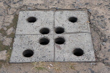 Balcony steel drain hole mesh and green leaves. Black metal Drainage grate for draining, directing excess water down into the sewers and prevent flooding. Dandelions sprouted between the tiles