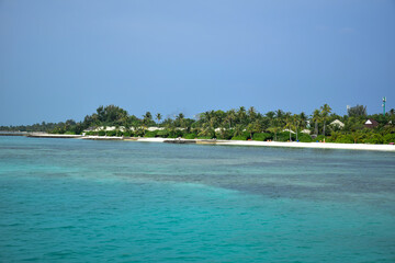 Maldives island landscape. Water, sand and greenery. Lush, tropical, vegetation, palm trees and bushes Shoreline with sandy beach. Wooden pathway pier. Walkway deck to private villas. Floating house