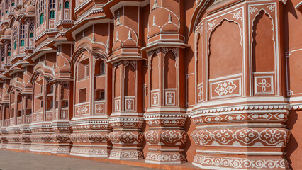 Details of the architecture of the ancient palace of the winds- Hawa Mahal. The red sandstone walls are decorated with white ornaments. Barred windows and balconies are visible. India. Jaipur