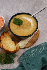 red lentils soup puree in dark bowl with bread on grey marble table