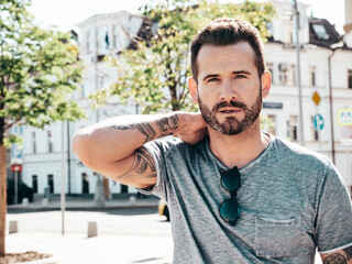 Portrait of handsome confident stylish hipster model. Sexy man dressed in jeans and grey t-shirt. Fashion male posing in the street. In Europe city. Outdoors at sunny day. With tattoos