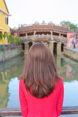 Fototapeta na wymiar Woman traveler wearing Ao Dai Vietnamese dress sightseeing at Japanese covered bridge in Hoi An town, Vietnam. landmark and popular for tourist attractions. Vietnam and Southeast Asia travel concept
