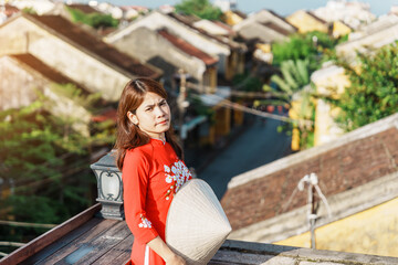 happy woman wearing Ao Dai Vietnamese dress, traveler sightseeing view at rooftop at Hoi An ancient town in Vietnam. landmark and popular for tourist attractions. Vietnam and Southeast travel concept