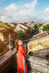 Fototapeta premium happy woman wearing Ao Dai Vietnamese dress, traveler sightseeing view at rooftop at Hoi An ancient town in Vietnam. landmark and popular for tourist attractions. Vietnam and Southeast travel concept