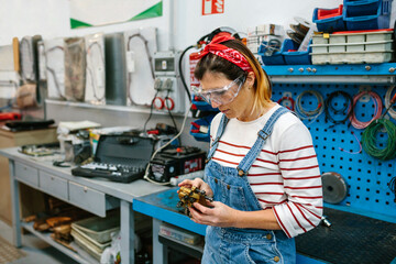 Portrait of mechanic woman with safety glasses checking caliper brake system in front of workbench on factory