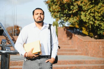 Male indian student standing at the university with book.