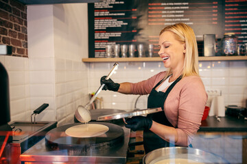 A pancake shop chef is baking crapes on hot plate and smiling at it.