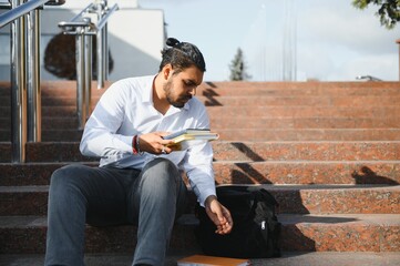 Happy indian student sitting on the stairs, in the university campus.