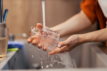 Close up of female's hands washing drinking glass in sink.
