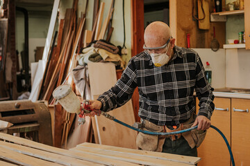 Carpenter using paint sprayer in workshop