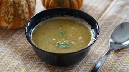 vegetable soup in a black bowl on a yellow-white placemat and two little pumpkins
