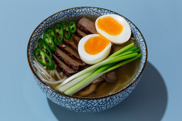 bowl of ramen with beef and eggs on blue background