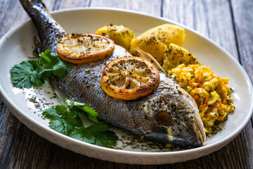 Roast sea bream with potatoes and vegetables on wooden table
