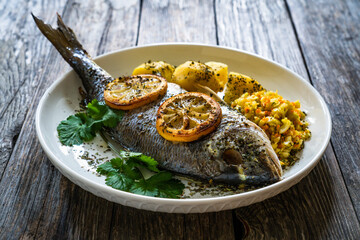 Roast sea bream with potatoes and vegetables on wooden table
