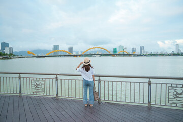 Woman Traveler visiting in Da Nang city. Tourist sightseeing the river view with Dragon bridge. Landmark and popular for tourist attraction. Vietnam and Southeast Asia travel concept
