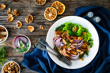 Marinated herrings with delicacies, walnuts and fresh vegetable leaves on wooden table
