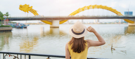 Woman Traveler with yellow dress visiting in Da Nang. Tourist sightseeing the river view with Dragon bridge at love lock bridge. Landmark and popular. Vietnam and Southeast Asia travel concept