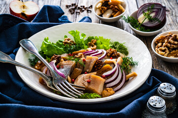 Marinated herrings with delicacies, walnuts and fresh vegetable leaves on wooden table
