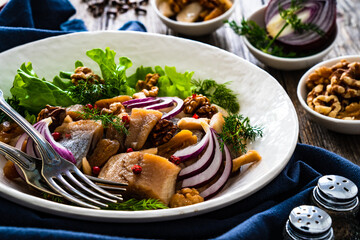 Marinated herrings with delicacies, walnuts and fresh vegetable leaves on wooden table
