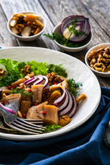 Marinated herrings with delicacies, walnuts and fresh vegetable leaves on wooden table
