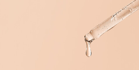 serum pipette close-up with falling drop on a beige background