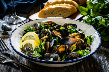 Cooked mussels with lemon and parsley on wooden table
