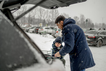 Father with son sitting in shopping cart at snowy parking lot