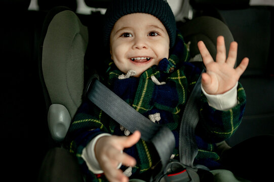 Smiling cute boy sitting in safety seat gesturing in car