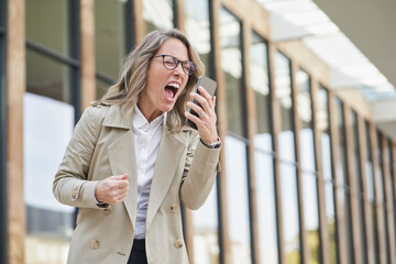 Mature businesswoman shouting on speaker phone outside building