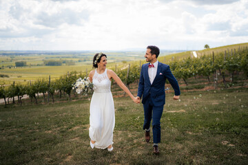 Wedding couple, groom is running while holding brides hand  in the vineyards of Rheinhessen