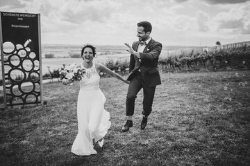 Wedding couple, groom is jumping while holding brides hand in black and white in the vineyards of...