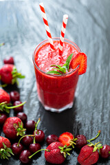 From above view of berry juice or smoothie with fresh strawberries and cherries on dark table.