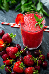 From above shot of berry smoothie in glass with fresh mint, strawberries, cherries black wood table