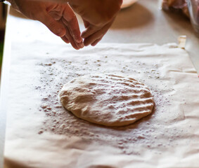 Cooking dough for pizza. The cook rolls out the dough and sips the flour