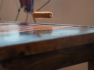 Close up of worker hand using a roller for painting a desk. House renovation concept.