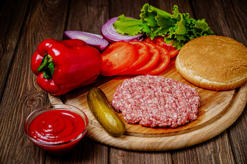 From above view of process of making burger with vegetables, bun and artificial meat on wooden board
