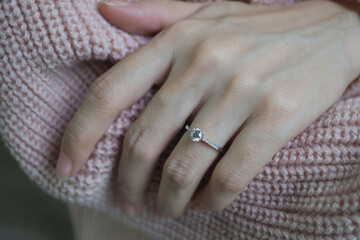 Close up of an elegant engagement diamond ring on woman finger with pink sweater winter clothe....