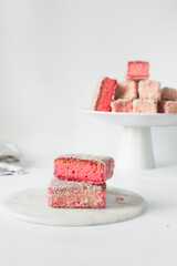 Pink lamingtons on a plate Australian raspberry lamingtons, small cakes covered in desiccated coconuts