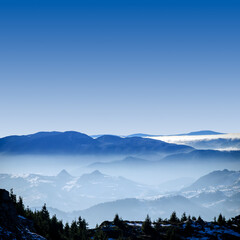 Obraz premium Foggy winter landscape in the mountains. Fantastic winter landscape. Aerial and morning view of snow covered mountain peaks rising over the foggy valleys. Dramatic overcast sky. Beauty world