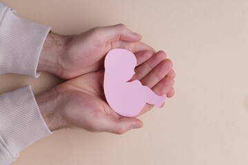 Female health. Man holding newborn paper figure on beige background, top view