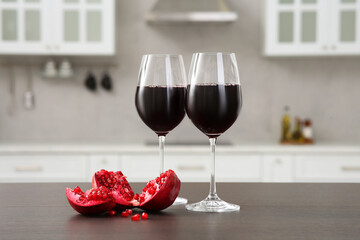Glasses of red wine and fresh pomegranate on countertop in kitchen