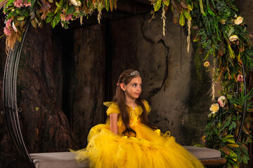 Smiling elegant stylish little princess in yellow dress sitting on bench in mystery decorated room....
