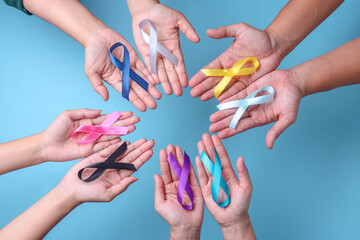 World cancer day. Hands of people open and holding colorful awareness ribbons forming circle as unity on blue background for supporting people living and illness. 