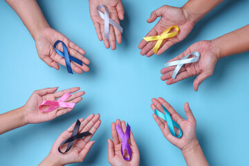 World cancer day. Hands of people open and holding colorful awareness ribbons on blue background for supporting people living and illness. 