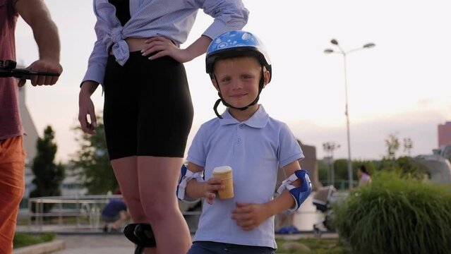 Close-up of a little boy eating ice cream, his parents are standing on an electric scooter.