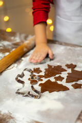 Close-up of a child's hand making a gingerbread cookie in the form of a Christmas tree and ginger man. Christmas and New Year concept
