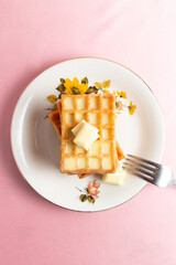 Top vertical view of a pile of belgian waffles with white chocolate on a pink background