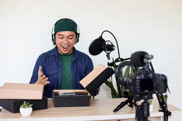 Asian man in casual style unboxing and reviewing product using professional podcast equipment.